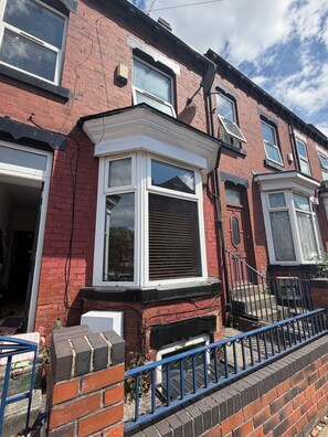 A red brick terraced house with a bay window, a front door, and a blue metal railing. - Boho Retro 4-bedroom house in charming Headingley for your Leeds stay (Leeds)