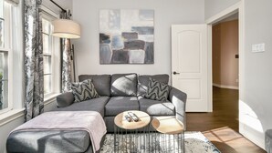 Una sala moderna con un sofá seccional gris, una mesa de centro y un cuadro abstracto grande en la pared.