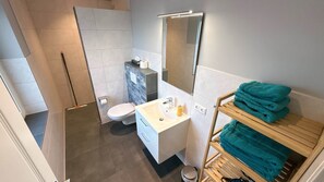 Moderni kylpyhuone, jossa on suihku, wc, pesuallas ja pyyheteline.