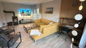 A living room with a sofa, coffee table, TV, fireplace, and a dining area. - Vacation home Inseltraum Bauernhof-Claussen (Fehmarn)