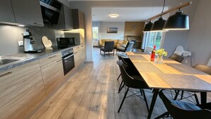 A modern kitchen with a central island, built-in appliances, and a dining area with a long table and chairs. - Vacation home Inseltraum Bauernhof-Claussen (Fehmarn)