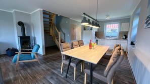 A modern kitchen with a wooden staircase, a dining area with a wooden table and cushioned seating, and a built-in wood-burning stove. - Vacation apartment Möwe Bauernhof-Claussen (Fehmarn)