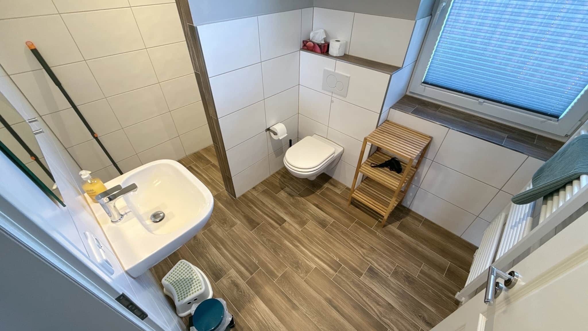 A bathroom with a sink, toilet, and wooden floor.