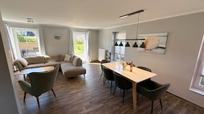 A modern living room with a sofa, dining table, chairs, and a view of the outdoors. - Vacation apartment Muschel Bauernhof-Claussen (Fehmarn)