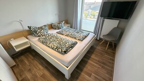 Ett modernt sovrum med en säng, sängbord, en stol, en tv och ett fönster med utsikt.