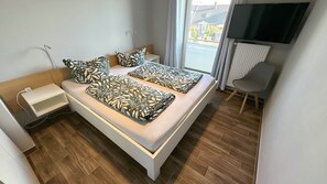 Ein modernes Schlafzimmer mit einem Bett, Nachttischen, einem Sessel, einem Fernseher und einem Fenster mit Blick.