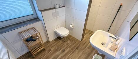 Une petite salle de bain avec des toilettes, un lavabo, un plancher en bois et une fenêtre avec des stores.