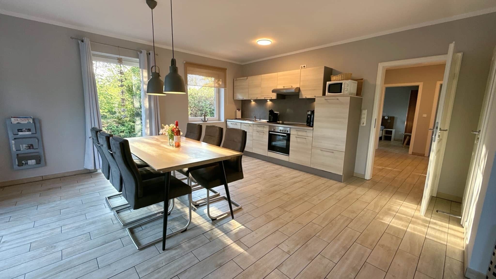 A modern kitchen with a dining area, wooden flooring, and pendant lighting.
