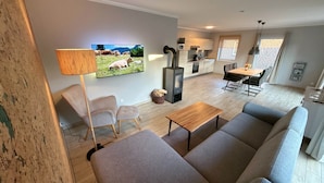 En moderne stue med sofa, bord, tv, pejs og et køkkenområde.