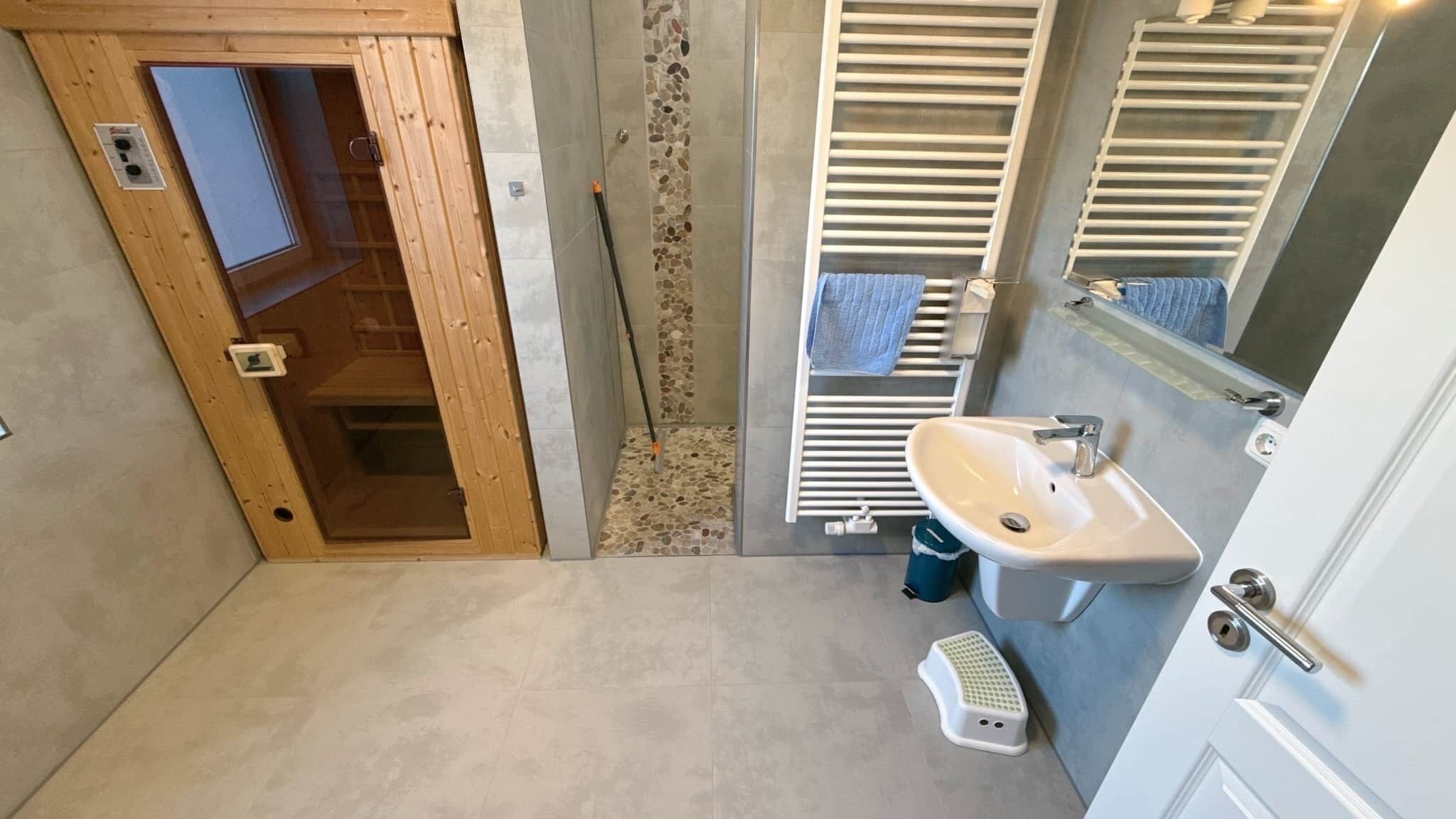 Une salle de bain avec une porte en bois, un lavabo blanc, un porte-serviettes et un espace douche.