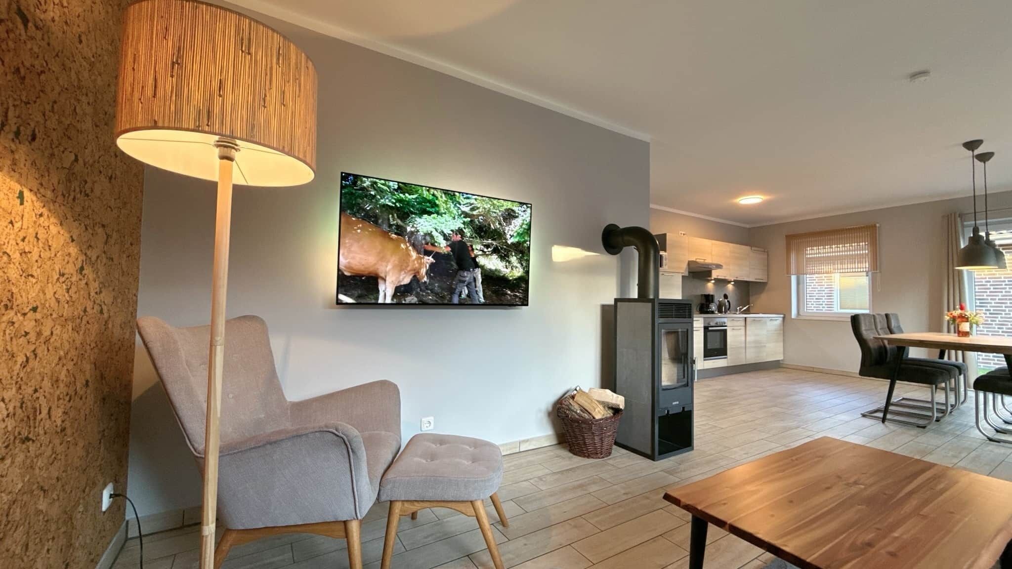 Ein modernes Wohnzimmer mit einer Couch, einem Couchtisch, einem an der Wand montierten Fernseher und einer Küchenzeile im Hintergrund.