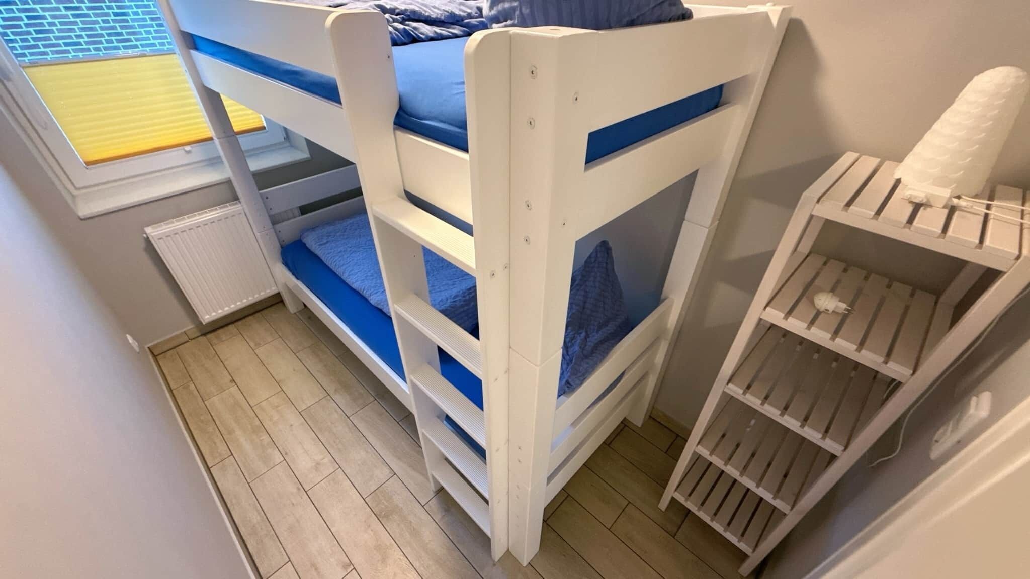 A bunk bed with a window, a radiator, and a small shelf unit.