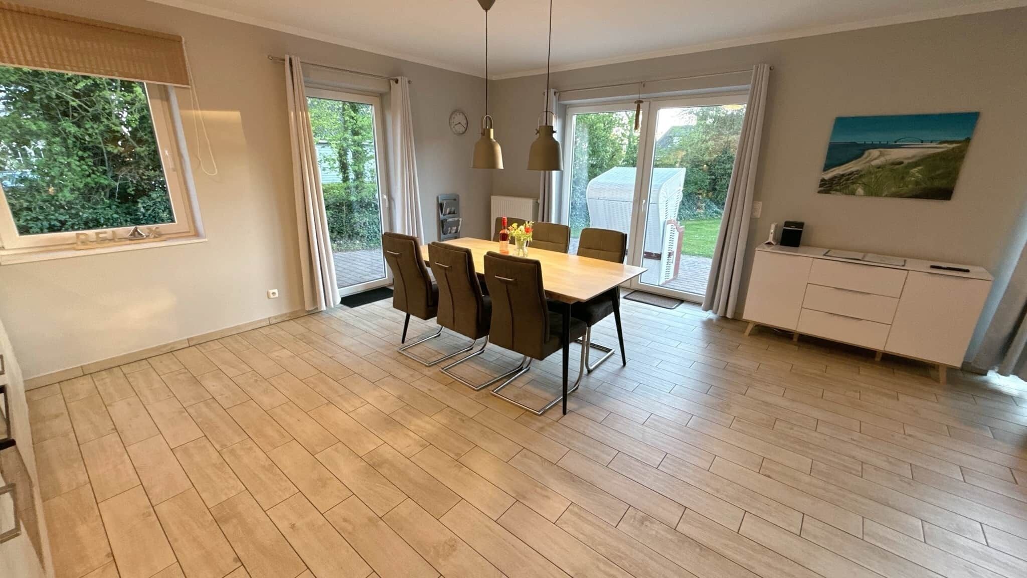 Un espace de salle à manger moderne avec une table et des chaises en bois, un meuble blanc et une vue sur la verdure à l’extérieur.