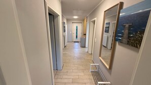 A hallway with a wooden floor, white walls, and a large mirror reflecting a painting. - Vacation cottage Sonne Bauernhof-Claussen (Fehmarn)