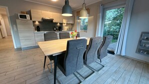 A modern kitchen with wooden cabinets, a dining table with chairs, and pendant lighting. - Vacation cottage Sonne Bauernhof-Claussen (Fehmarn)