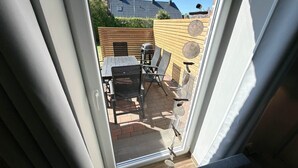 A patio with a table and chairs, a grill, and a wooden fence. - Vacation apartment Welle Bauernhof-Claussen (Fehmarn)