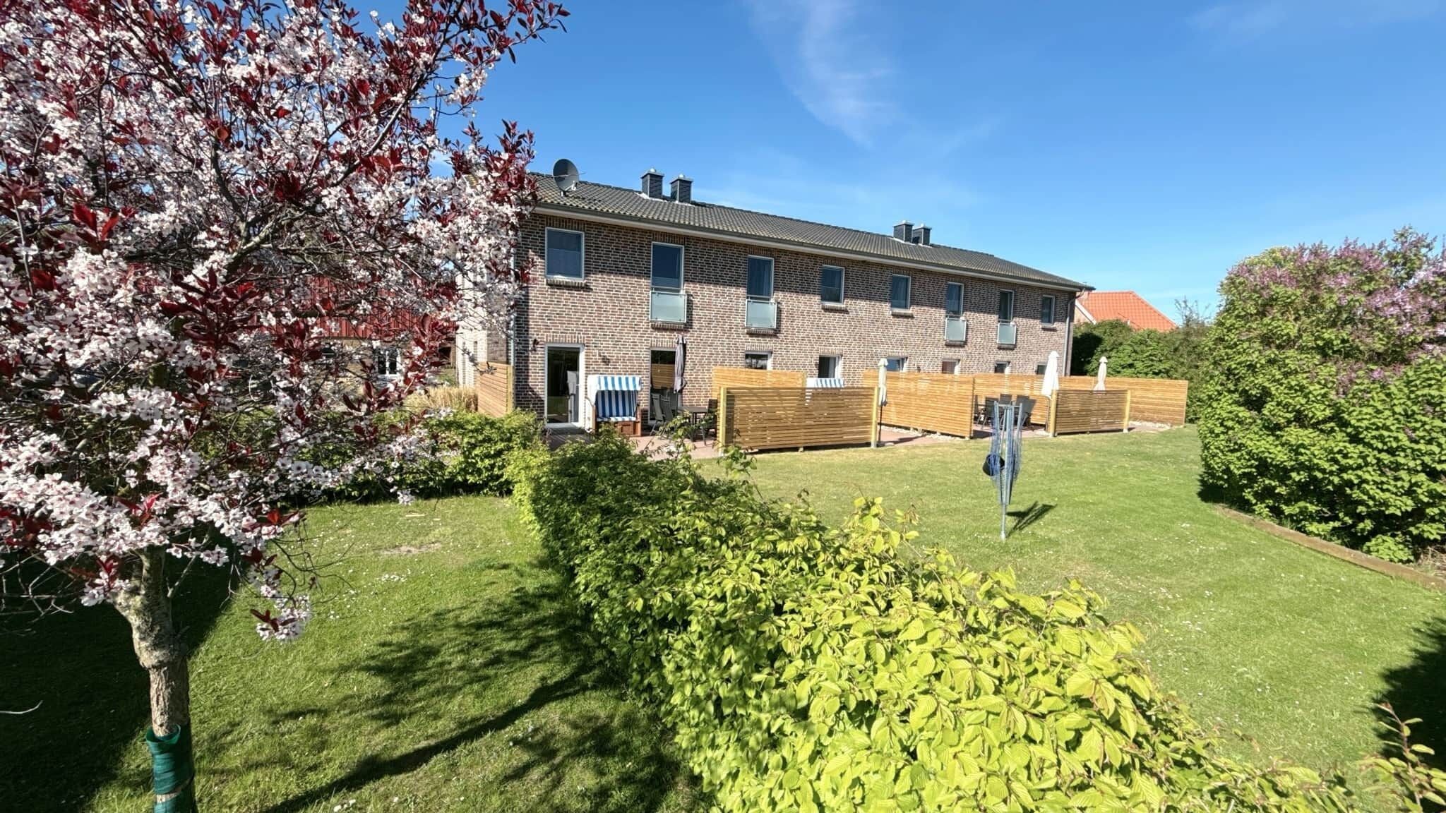 A two-story brick building with a well-maintained lawn, a wooden fence, and flowering trees.
