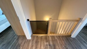 A narrow staircase with a glass door leading to a room. The floor is tiled with a dark wood pattern. - Vacation apartment Welle Bauernhof-Claussen (Fehmarn)