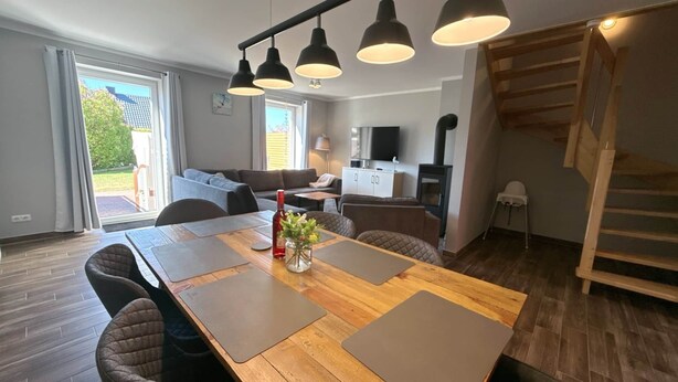 A modern living room with a wooden dining table, cushioned chairs, a sofa, a TV, and a fireplace. - Vacation apartment Welle Bauernhof-Claussen (Fehmarn)