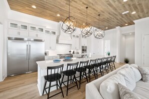 A modern kitchen with white cabinets, a stainless steel refrigerator, and a central island with bar stools. - Huge Corner House 30A! Free Bikes/Walk to Beach! (Santa Rosa Beach)