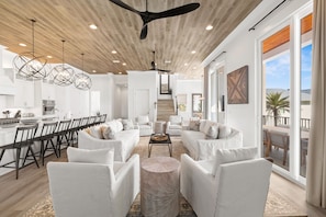 A modern kitchen with white cabinets, a dining area with a long table and chairs, a living room with white sofas and a coffee table, and a large sliding glass door to the outside. - Huge Corner House 30A! Free Bikes/Walk to Beach! (Santa Rosa Beach)