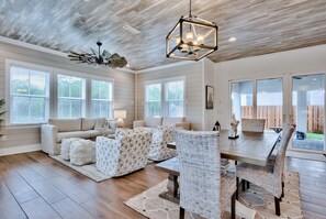 A spacious living room with a wooden ceiling, large windows, a dining area with wicker chairs, and a ceiling fan. - Private Pool/Free Bikes! 0.7 Miles from Beach. (Santa Rosa Beach)