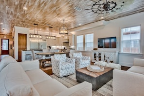 A spacious living room with a wooden ceiling, a dining area with a kitchen in the background, and a large window providing natural light. - Private Pool/Free Bikes! 0.7 Miles from Beach. (Santa Rosa Beach)