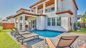 Una casa de dos pisos con piscina, mobiliario exterior y un patio cubierto.