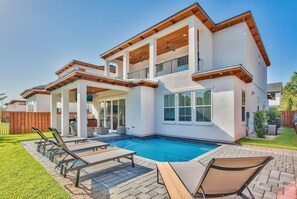 Ein zweistöckiges Haus mit Swimmingpool, Sitzgelegenheiten im Freien und einer überdachten Terrasse.