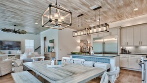 Una cocina amplia con una isla grande, electrodomésticos modernos y un comedor con mesa de madera y sillas blancas.