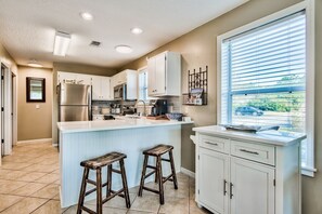 A kitchen with white cabinets, a stainless steel refrigerator, a large window with blinds, and two wooden stools. - Pet Friendly! Seagrove 30A! 1st Floor. Pool/Tennis! (Santa Rosa Beach)