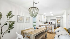 Een moderne keuken met witte kasten, een houten eettafel en een hanglamp.