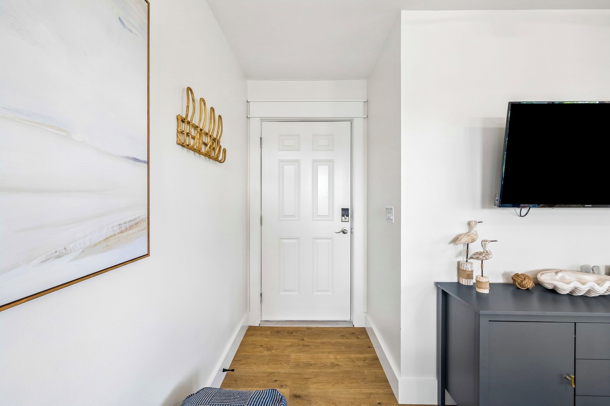 A hallway with a white door, a mounted television, and a dark-colored cabinet with decorative items.