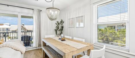 Une pièce moderne avec une table à manger en bois, des chaises blanches, un lustre et un balcon offrant une vue sur les bâtiments.