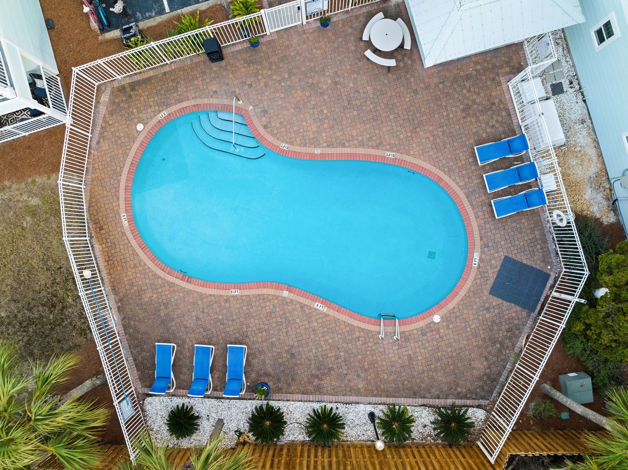 Vue aérienne d’une piscine entourée d’une terrasse, de chaises longues et d’un petit espace salon.