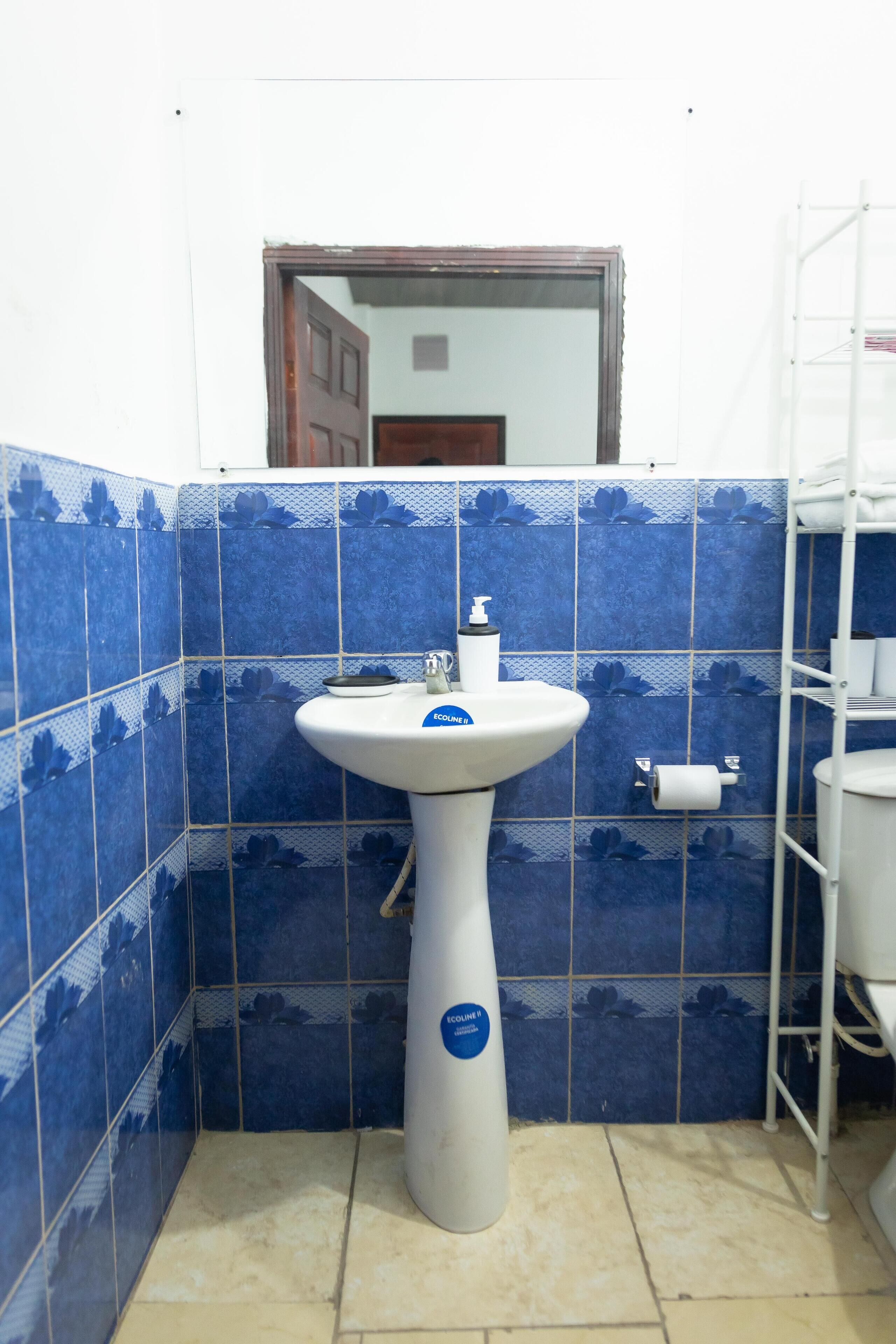 Um banheiro com pia branca, azulejos florais azuis, vaso sanitário branco e um armário branco.