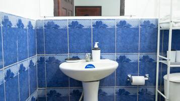 A bathroom with a white pedestal sink, blue floral tiles, a white toilet, and a white shelf unit.