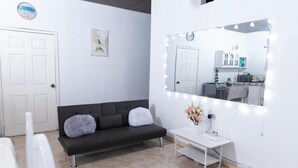 A room with a dark-colored sofa, a white vanity with a mirror, and a clock on the wall. - La Casona Blanca (San Marcos)