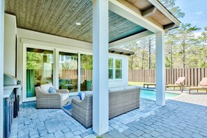 An outdoor patio with wicker furniture, a pool, and a wooden ceiling.