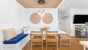 Un comedor con una mesa blanca, sillas de madera y un banco azul.