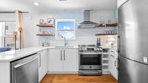 Una cocina moderna con armarios blancos, un refrigerador de acero inoxidable, horno empotrado y ventana con vista al cielo.