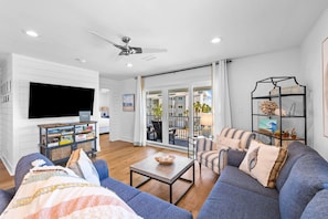Ein geräumiges Wohnzimmer mit einem großen Flachbildfernseher, einem Deckenventilator und einem Balkon mit Blick auf die Stadt.