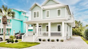 Une maison à deux étages avec un porche, des balustrades blanches et une allée pavée en briques.