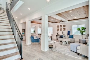 A spacious living area with a staircase, wooden flooring, and modern furniture. - 30A Family House! Free Bikes. Walk to Coffee/Dinner! (Santa Rosa Beach)