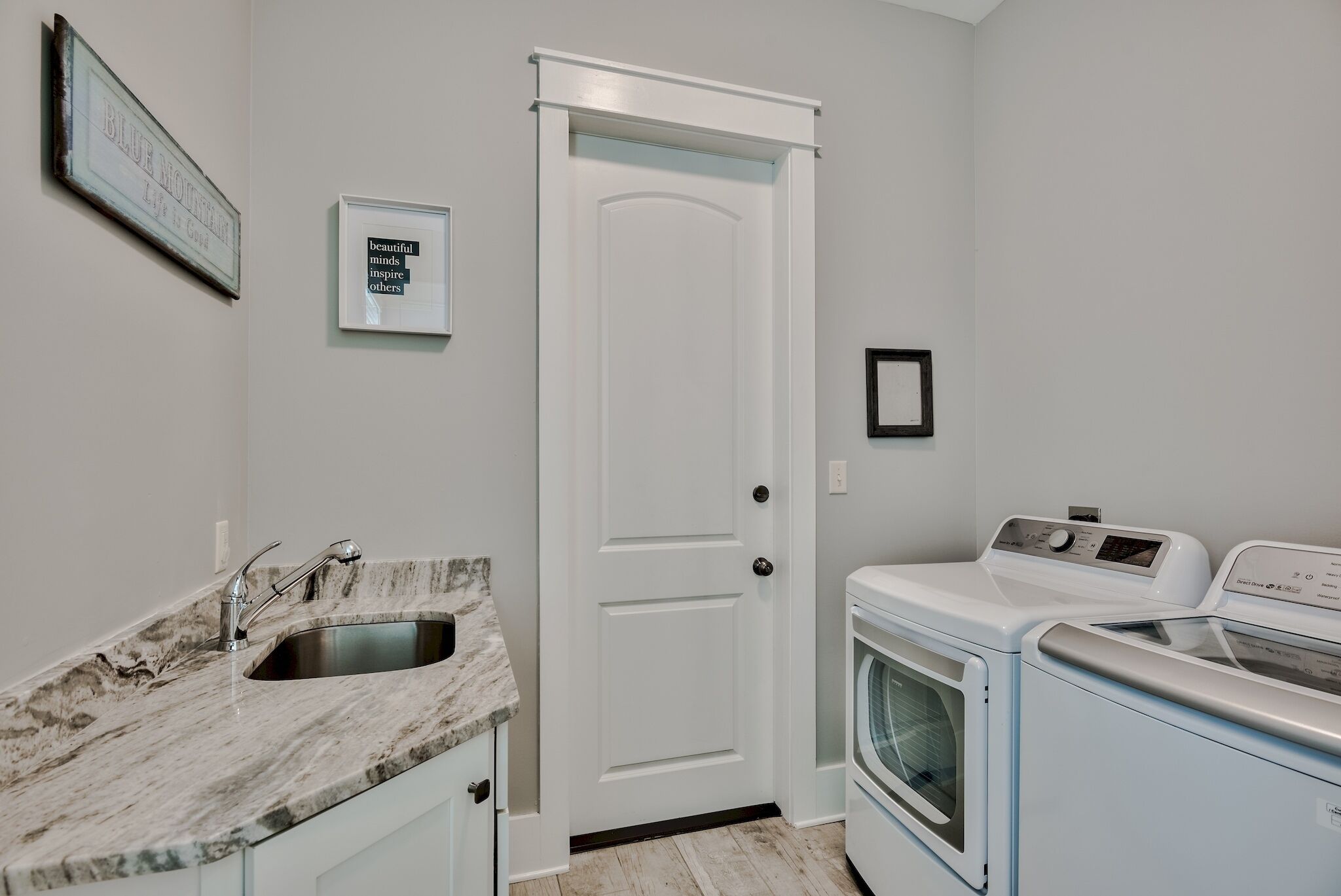 A kitchen with a marble countertop, a sink, a white door, and a white washing machine.