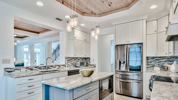 Une cuisine moderne avec des meubles blancs, un grand îlot central, des appareils en acier inoxydable et des luminaires suspendus.