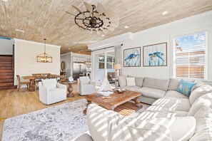 Ein geräumiges Wohnzimmer mit Holzboden, einer großen Couch, einem Couchtisch und einem Essbereich mit Holzmöbeln.