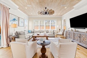A spacious living room with a modern ceiling fan, a large flat-screen TV, and a comfortable seating area with a sofa and armchairs. - Gulf Place 30A! Private Pool/Free Bikes. Families! (Santa)