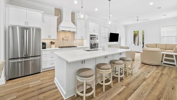 Una cocina moderna con armarios blancos, electrodomésticos de acero inoxidable y una isla central con taburetes.