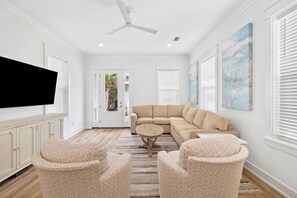 A spacious living room with a beige sectional sofa, two patterned armchairs, a round coffee table, a ceiling fan, and a flat-screen TV mounted on the wall. - Private Pool/Golf Cart! Bikes. 5 minute walk to Beach! (Santa Rosa Beach)